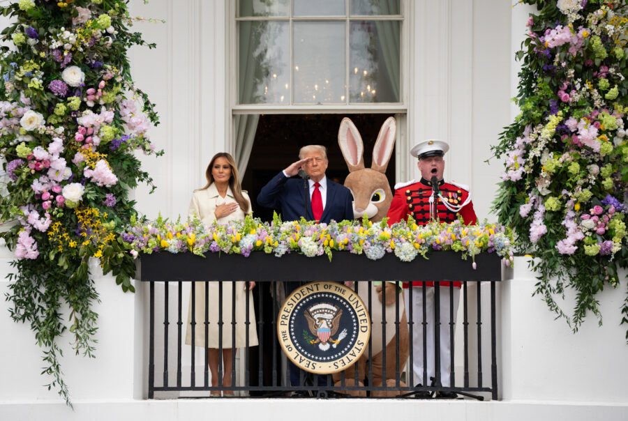 President Trump stands on the south balcony of the White House with his wife, Melania a person in an Easter Bunny suit, and a singing Marine. The annual Easter Egg Roll took place on the Monday of Trump's 14th week back in the White House.
