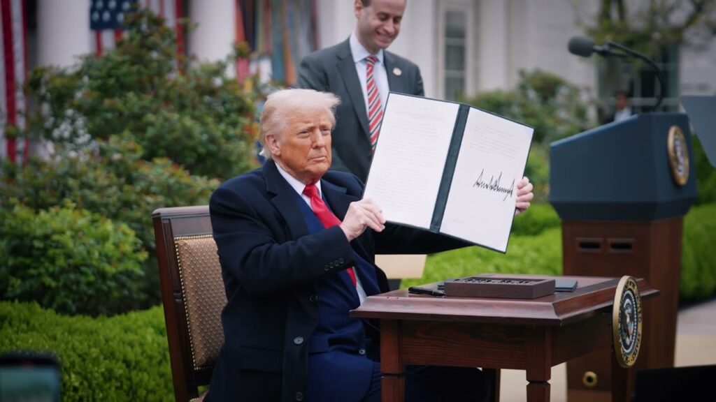 President Donald Trump, seated in the Rose Garden while holding a signed executive order imposing tariffs on virtually every U.S. trading partner. Trump officials traded stocks on their insider knowledge ahead of the tariff announcements, allowing them to skirt losses in the stock market panic that followed.